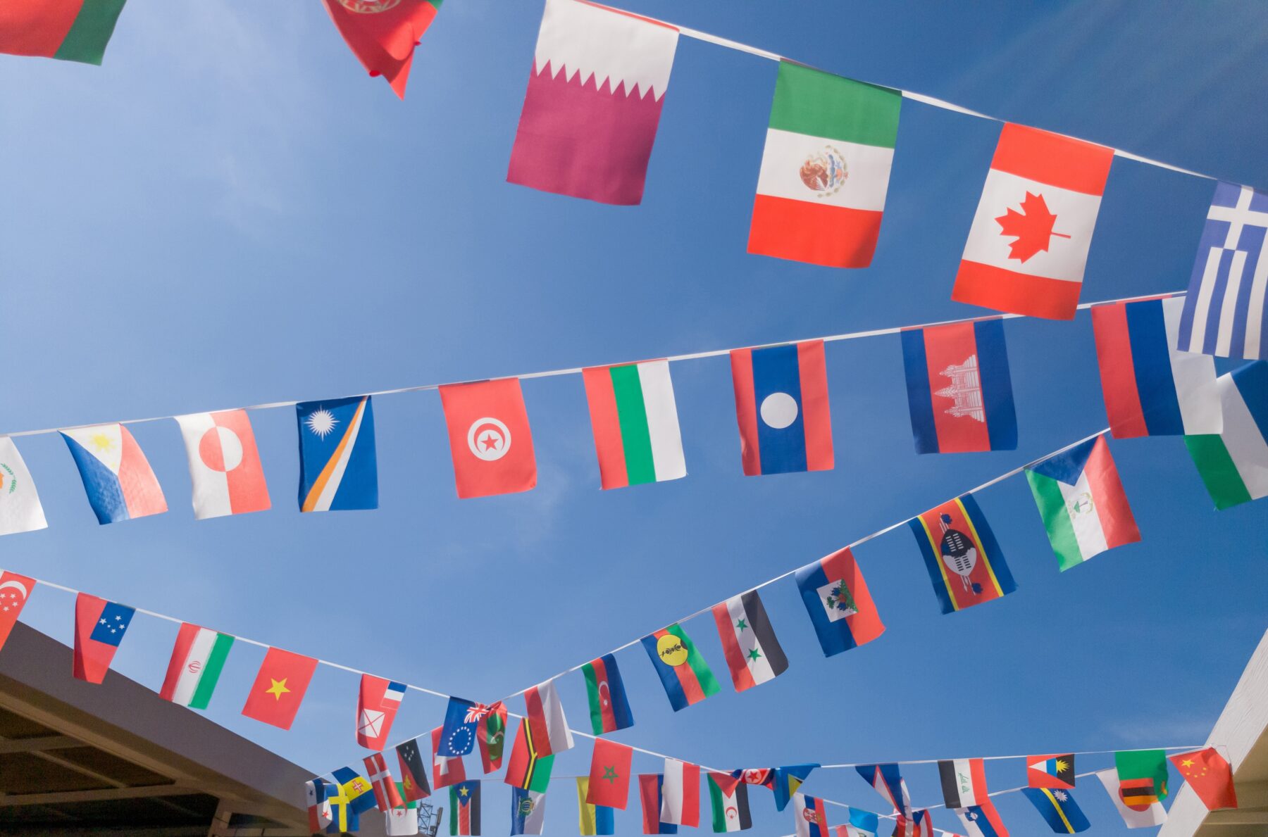 International flags from various nations hang on bunting lines against clear vibrant blue sky